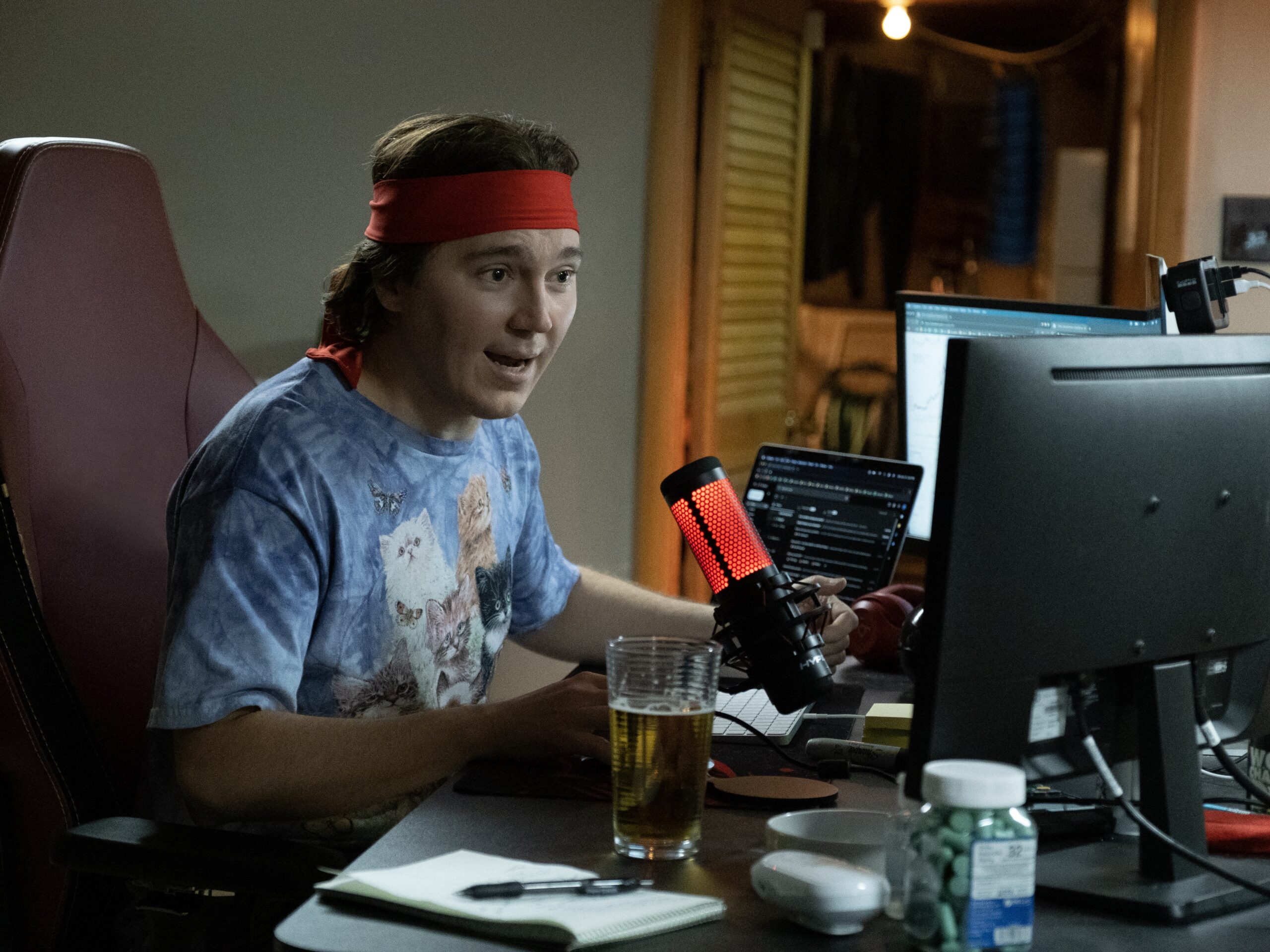 Ο Paul Dano κάθεται στο γραφείο του, μπροστά από μία οθόνη υπολογιστή και ένα μικρόφωνο.