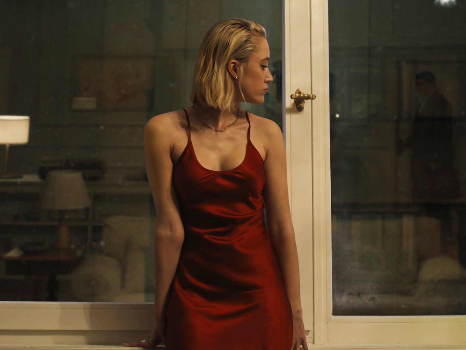 Η Maika Monroe ως Julia στέκεται μπροστά από το παράθυρο του διαμερίσματος της, φορώντας ένα κόκκινο νυχτικό.