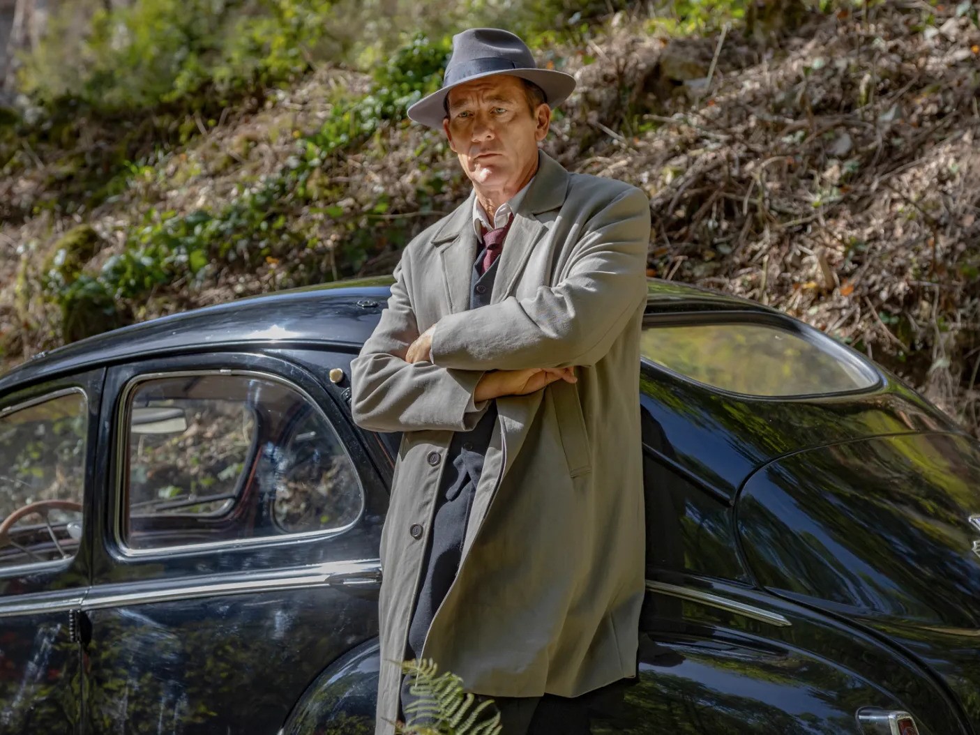 Ο Clive Owen ως Sam Spade στέκεται μπροστά από ένα αυτοκίνητο.