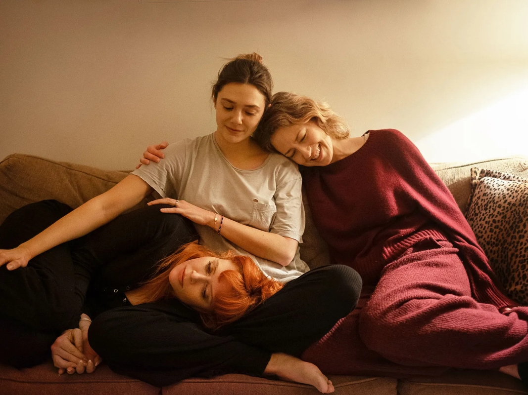 Από αριστερά προς τα δεξιά: Οι Natasha Lyonne, Elizabeth Olsen και Carrie Coon κάθονται αγκαλιασμένες στον καναπέ. Στιγμιότυπο από τη νέα ταινία του Azazel Jacobs, «His Three Daughters».